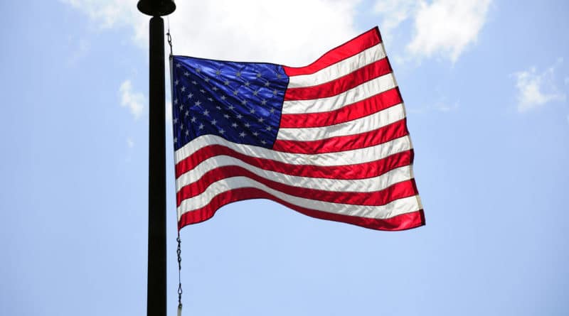 American flag waving on a flagpole against a blue sky.