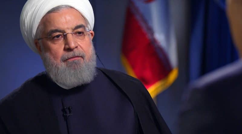 Portrait of a man in traditional attire with an Iranian flag in the background.