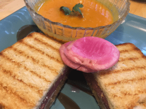 Grilled sandwich with creamy tomato soup and a slice of radish.