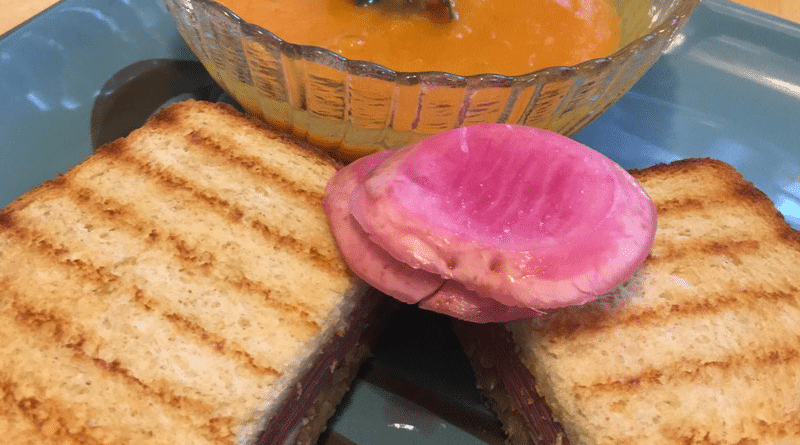 Grilled sandwich with creamy tomato soup and a slice of radish.