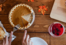 A person serving a slice of pumpkin pie at a wooden table with autumn leaves.