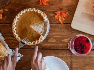 A person serving a slice of pumpkin pie at a wooden table with autumn leaves.