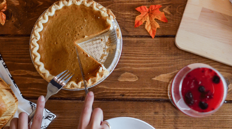 A person serving a slice of pumpkin pie at a wooden table with autumn leaves.