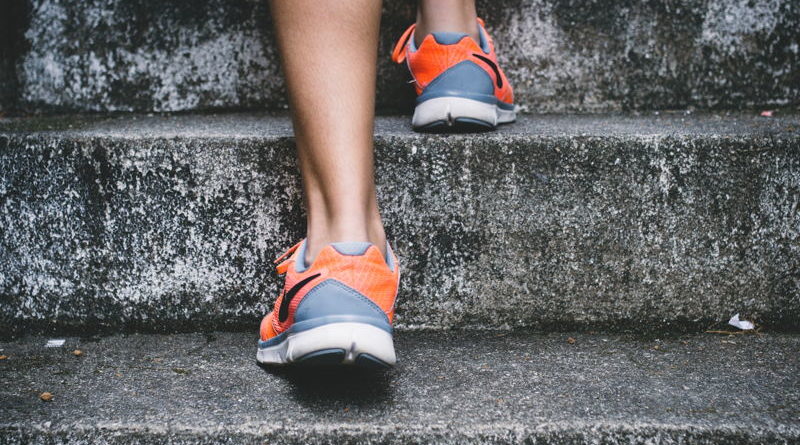 Person wearing orange and gray shoes walking up concrete stairs.