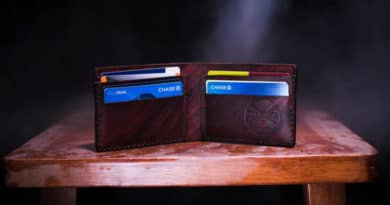 Open brown leather wallet with cards inside on wooden surface.