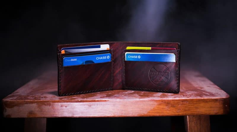 Open brown leather wallet with cards inside on wooden surface.