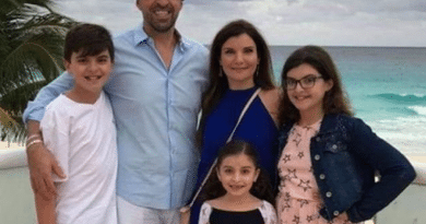 A family of five posing on a beach with cloudy skies.