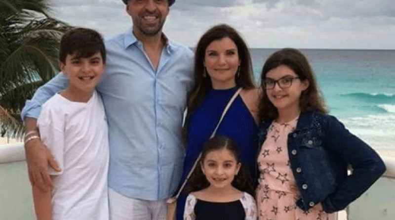 A family of five posing on a beach with cloudy skies.
