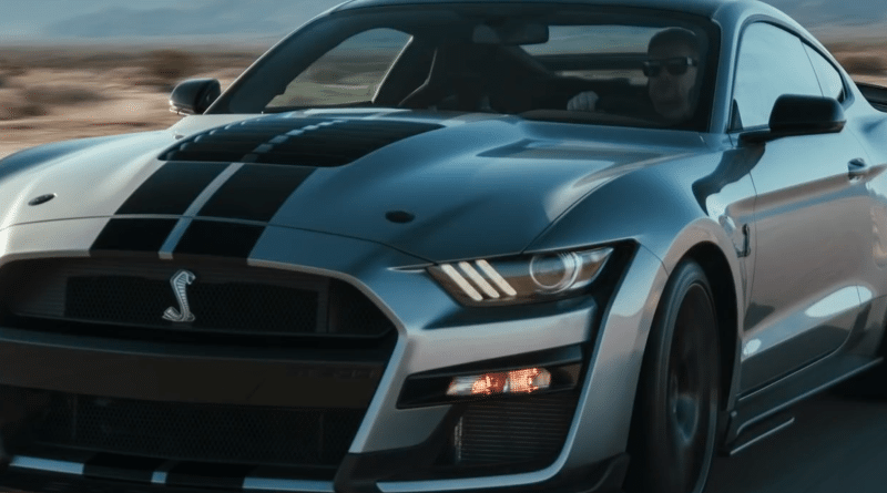 A sleek black sports car with racing stripes on the road.