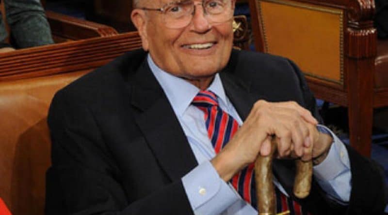 Elderly man smiling warmly while sitting indoors with a cane.
