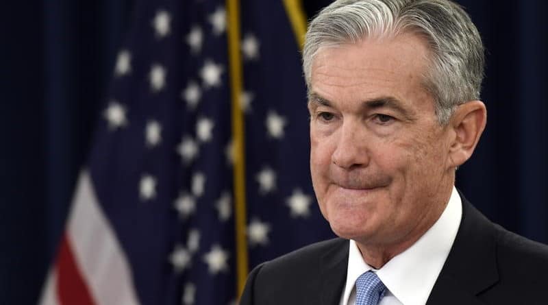 A man in a suit stands in front of American flags.