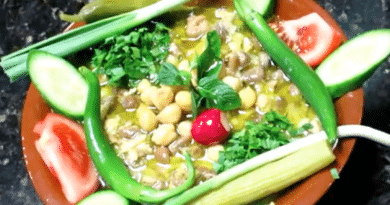 A colorful vegetable platter with fresh cucumber, tomato, and herbs around a chickpea dip.