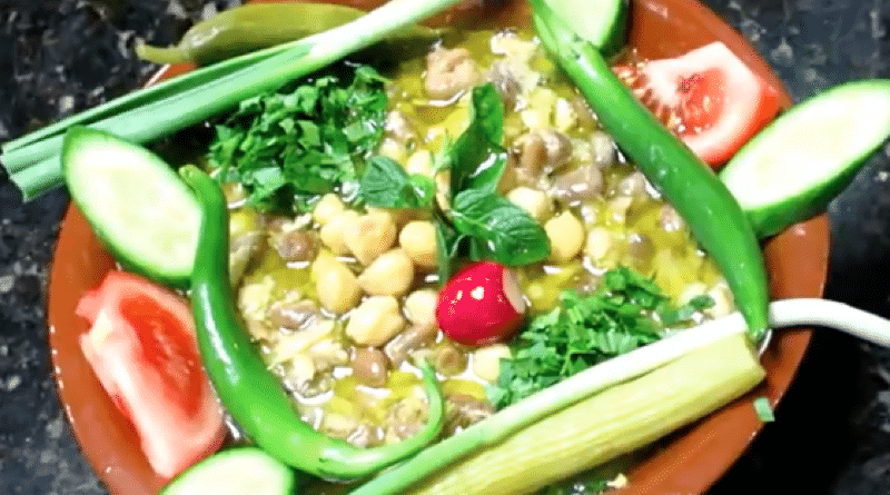 A colorful vegetable platter with fresh cucumber, tomato, and herbs around a chickpea dip.