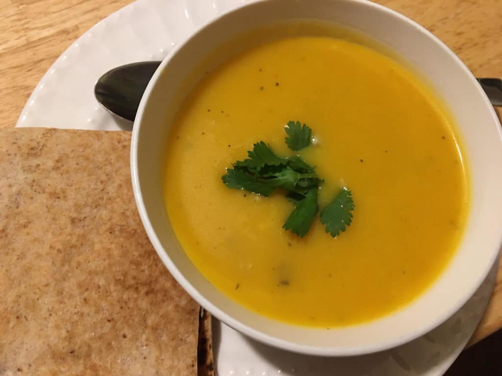 A bowl of creamy pumpkin soup garnished with cilantro, served with toasted bread.