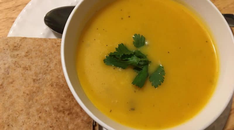 A bowl of creamy pumpkin soup garnished with cilantro, served with toasted bread.