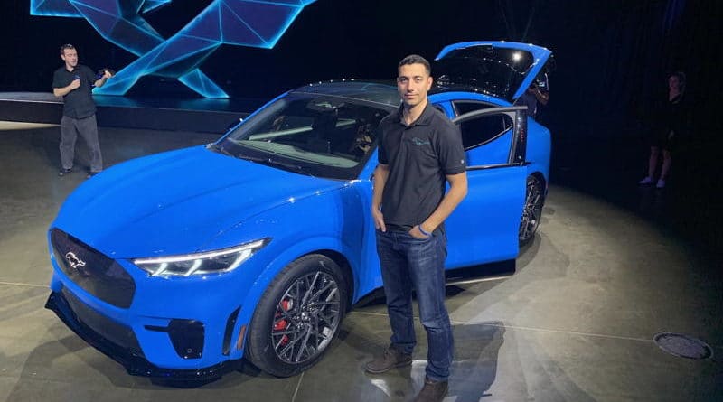 Man standing beside a blue sports car at an event.