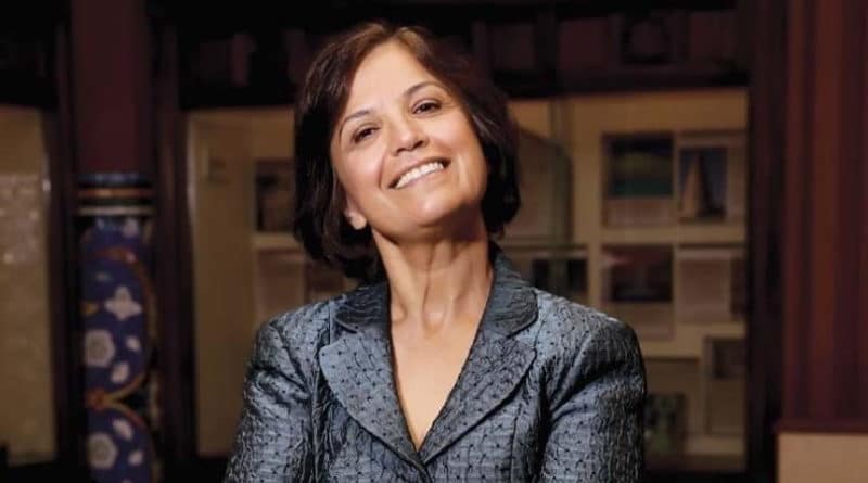 Smiling woman in a gray blazer with a confident pose.