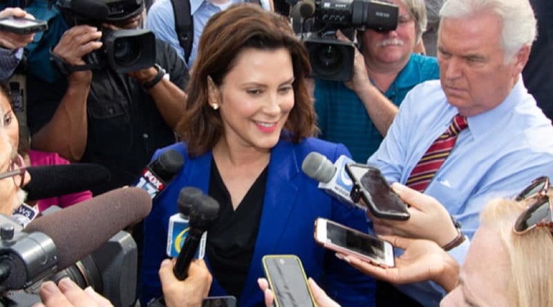 Woman surrounded by reporters and microphones at a press event.