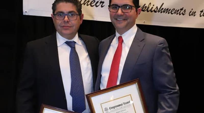 Two men in suits holding framed certificates and smiling.