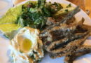 A plate with grilled fish, greens, and mashed potatoes with a yolk on top.