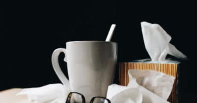 A coffee mug, glasses, and tissues on a table against a dark background.