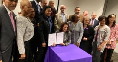 Group photo with a woman signing a document at a purple-covered table.