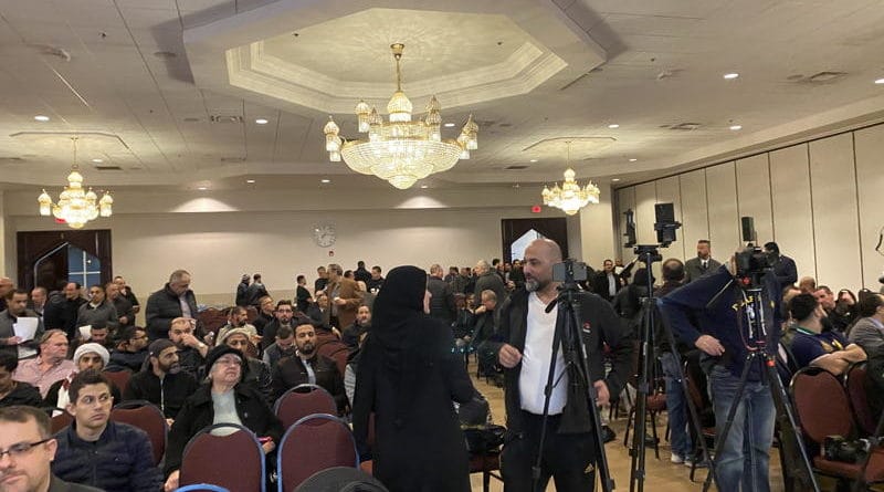 A crowded conference room with attendees and media personnel.