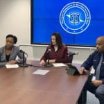 Three professionals in a meeting room with a presentation screen.