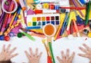 Children's hands with colorful art supplies and paints on a table.