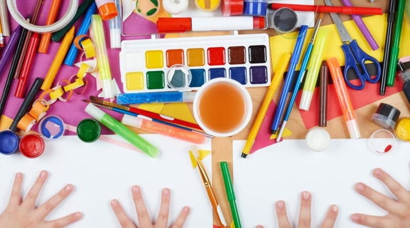 Children's hands with colorful art supplies and paints on a table.