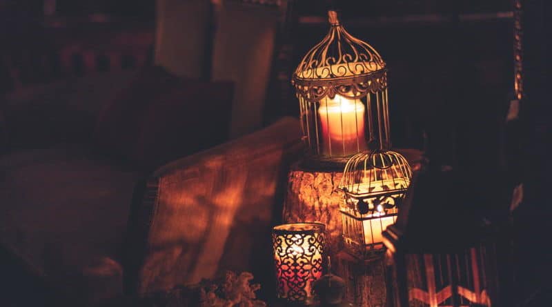 Warm candlelight glowing inside ornate lanterns in a dim setting.