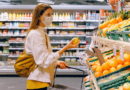 Woman shopping for oranges in a grocery store while wearing a face mask.