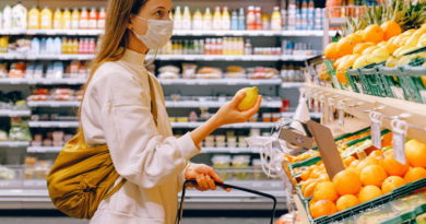Woman shopping for oranges in a grocery store while wearing a face mask.