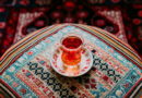 A glass of tea on a saucer sits on a patterned tablecloth.