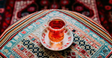 A glass of tea on a saucer sits on a patterned tablecloth.