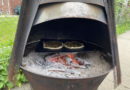 Two pizzas baking inside a wood-fired oven with glowing embers.