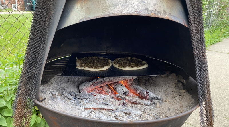 Two pizzas baking inside a wood-fired oven with glowing embers.