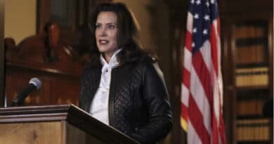 A woman speaks at a podium with an American flag behind her.