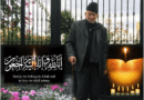 Elderly man in black coat and hat standing beside Islamic calligraphy outdoors.