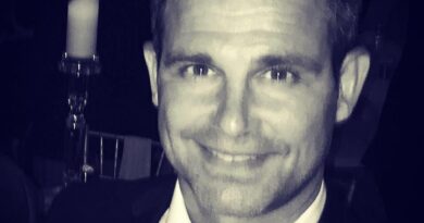 Smiling man in a suit with a candlelit background.