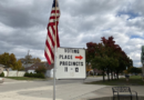 Sign indicating voting place and precincts with American flag.