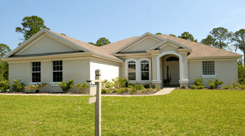 A white house with a large front yard and mailbox on a sunny day.