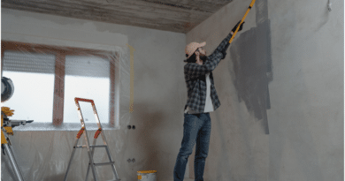 A person painting a wall gray in a room under renovation.