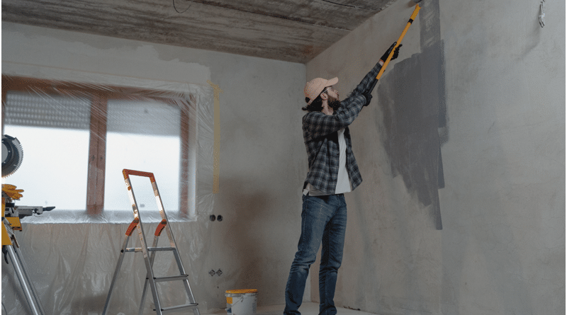 A person painting a wall gray in a room under renovation.