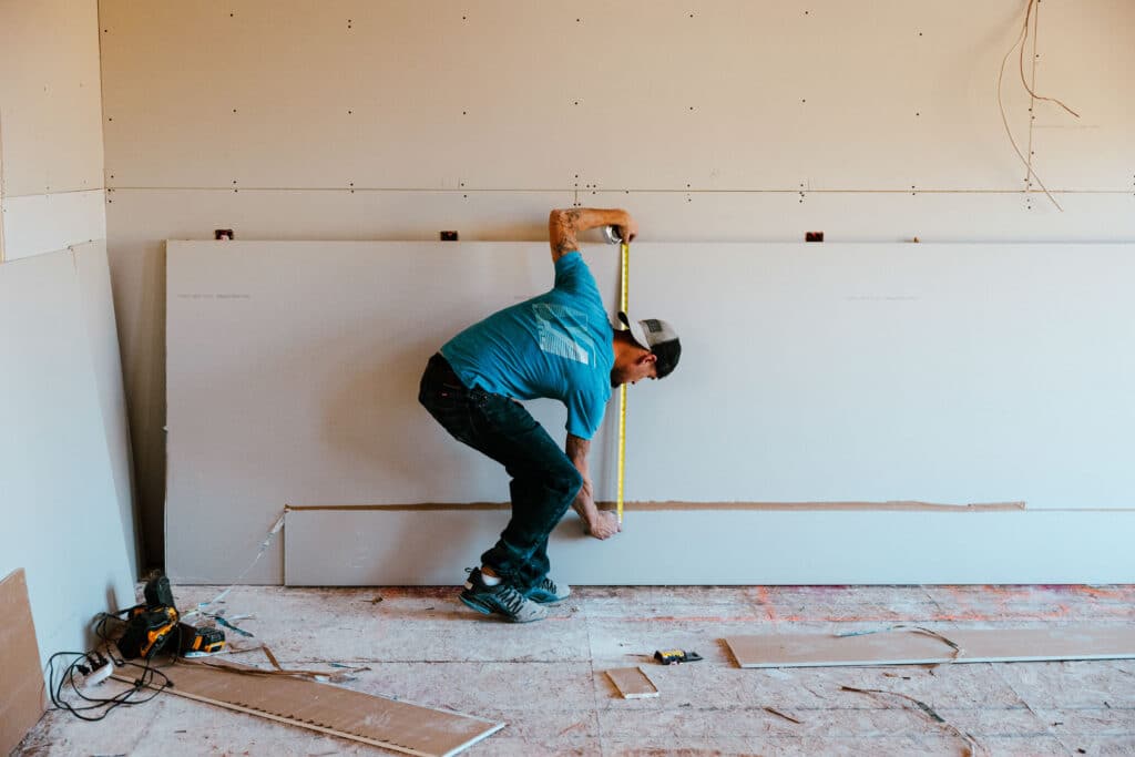 Man crouching indoors, touching the floor in a casual pose.