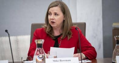 A woman in a red blazer speaking at a conference table.