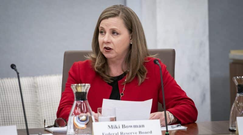 A woman in a red blazer speaking at a conference table.