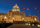 Illuminated government building with dome and flags at night.